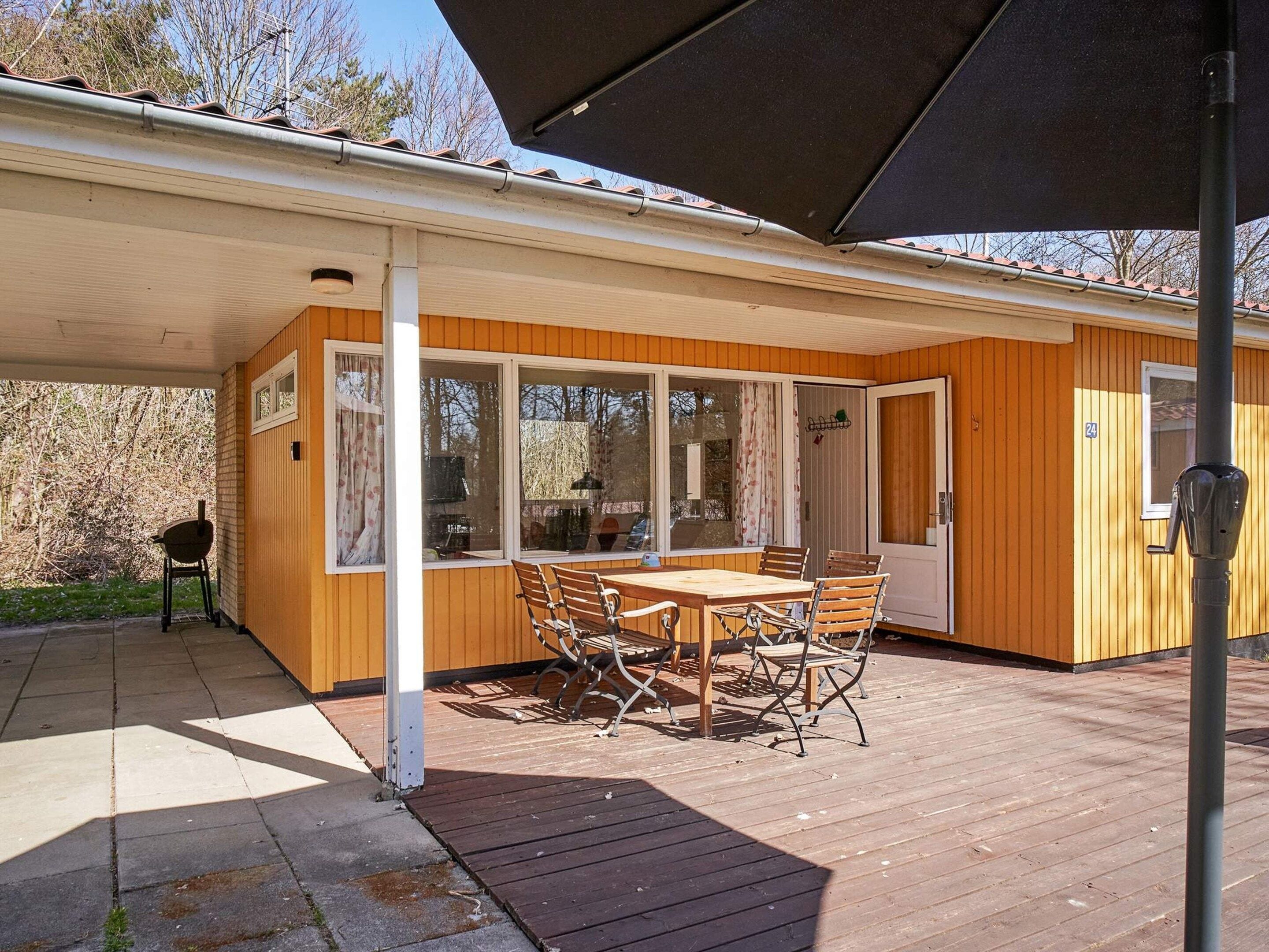 A covered outdoor area with a wooden deck, a table with chairs, and a door.