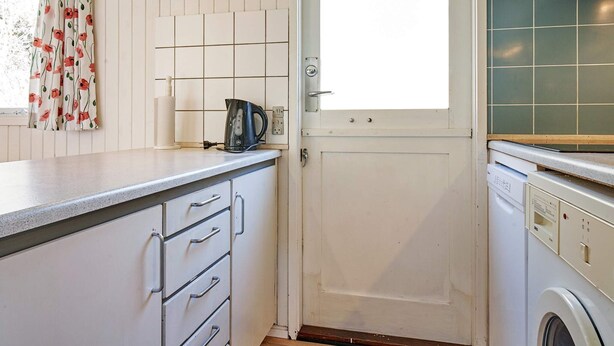 A kitchen with white cabinets, a kettle, a window with curtains, and a washing machine. - 4 Person Holiday Home in Aakirkeby (Akirkeby)
