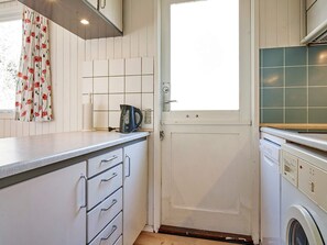 A kitchen with white cabinets, a kettle, a window with curtains, and a washing machine. - 4 Person Holiday Home in Aakirkeby (Akirkeby)