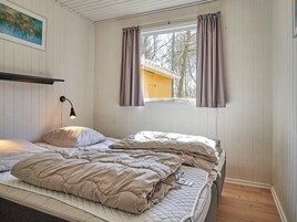 Un dormitorio con cama, mesita de noche, lámpara de pared y ventana con cortinas.