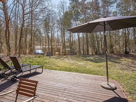 Una terraza de madera con muebles de exterior, incluyendo un banco y sillas, y una sombrilla grande que da sombra.