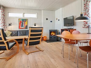Een knus woongedeelte met een houten vloer, een bank, een eettafel met stoelen, een open haard en een televisie.