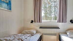 A small, single-room accommodation with two beds, a window with curtains, a radiator, and a wall-mounted light fixture. - 4 Person Holiday Home in Aakirkeby (Akirkeby)