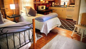 A cozy cabin-style room with two beds, a kitchenette, and wooden walls.