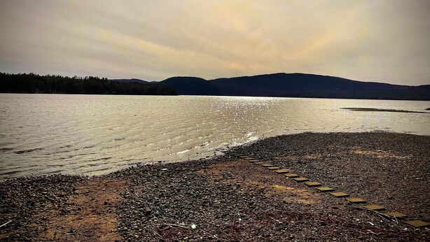 A lakeside view with a pebbled shore and distant mountains.