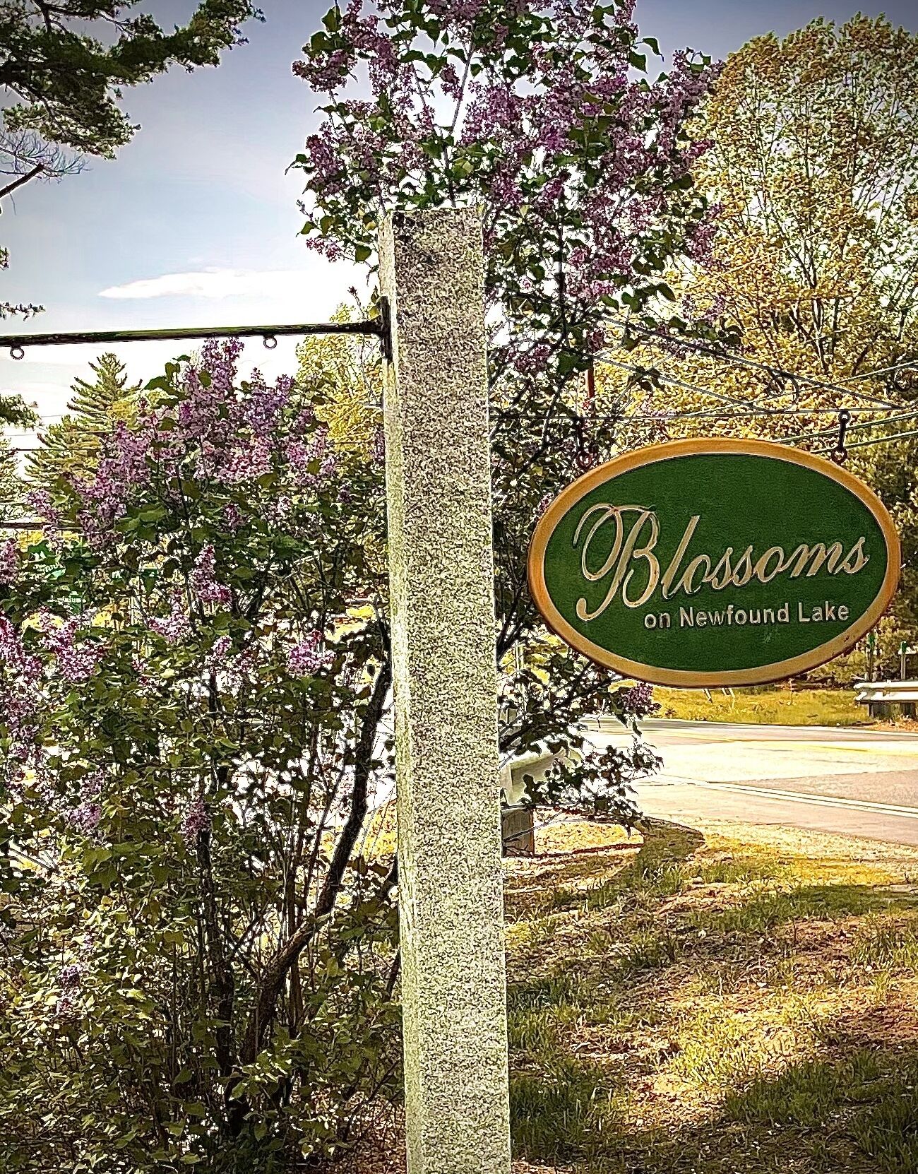 Une enseigne indiquant « Blossoms on Newfound Lake », avec un fond vert et des lettres blanches, fixée sur un pilier en pierre.