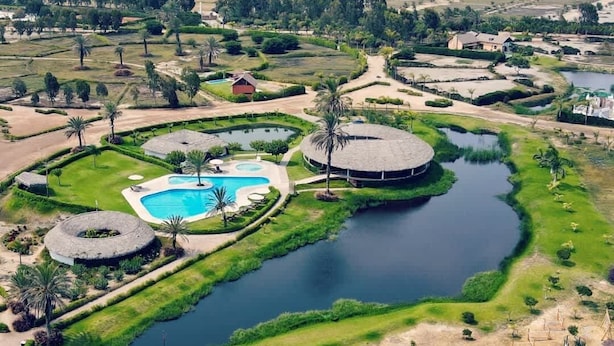 Vista aérea de un resort con una piscina central, fuentes de agua circulares y palmeras.