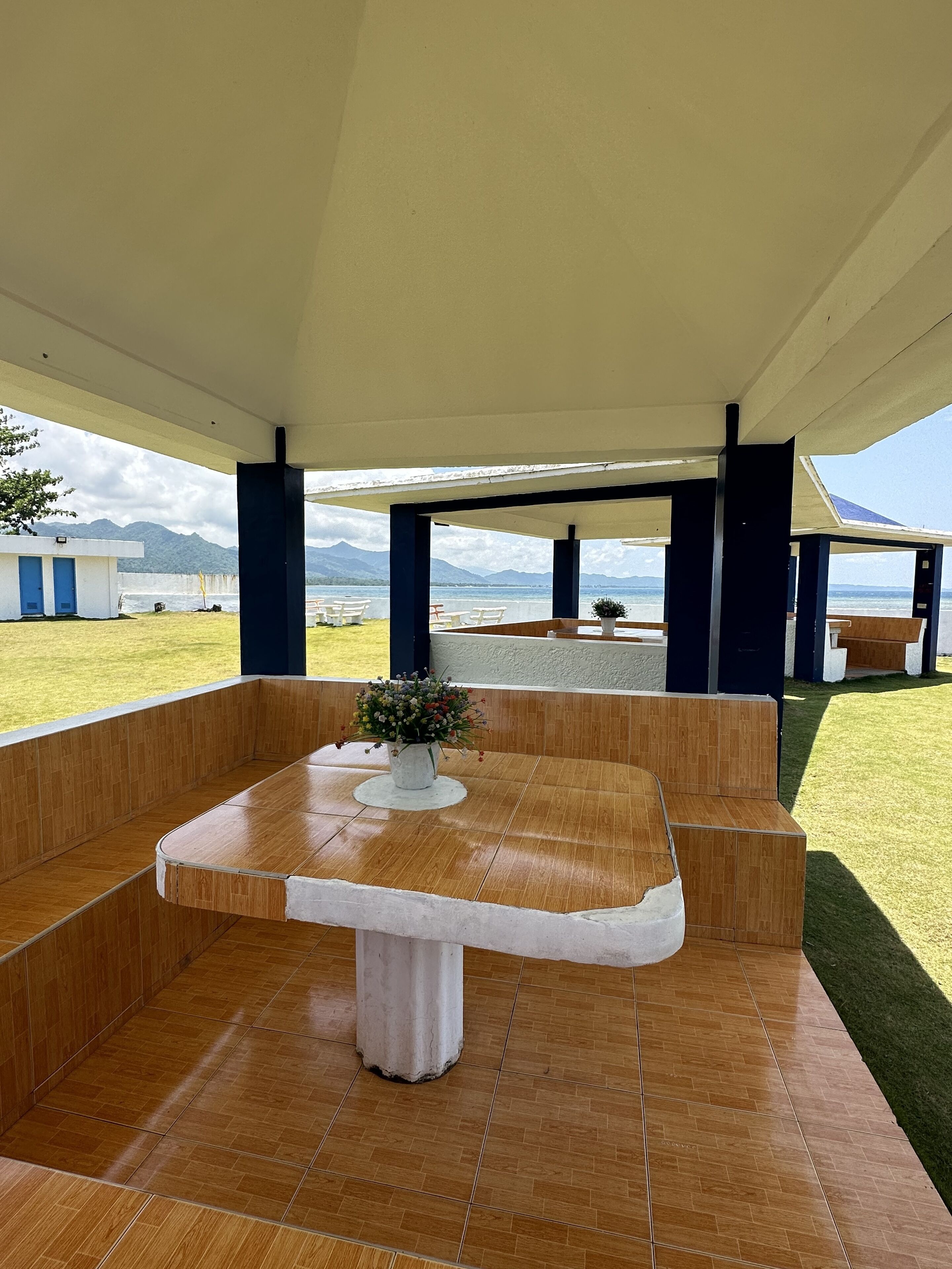 Un espacio al aire libre con mesas y bancos, una planta en maceta y vistas al mar y a las montañas.