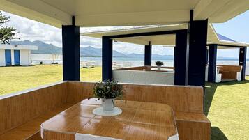 Un espacio al aire libre con mesas y bancos, una planta en maceta y vistas al mar y a las montañas.