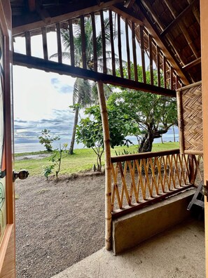 A wooden balcony with a view of a grassy area and a tree, overlooking a body of water. - Emmalyn's Paradise Resort (San Andres)