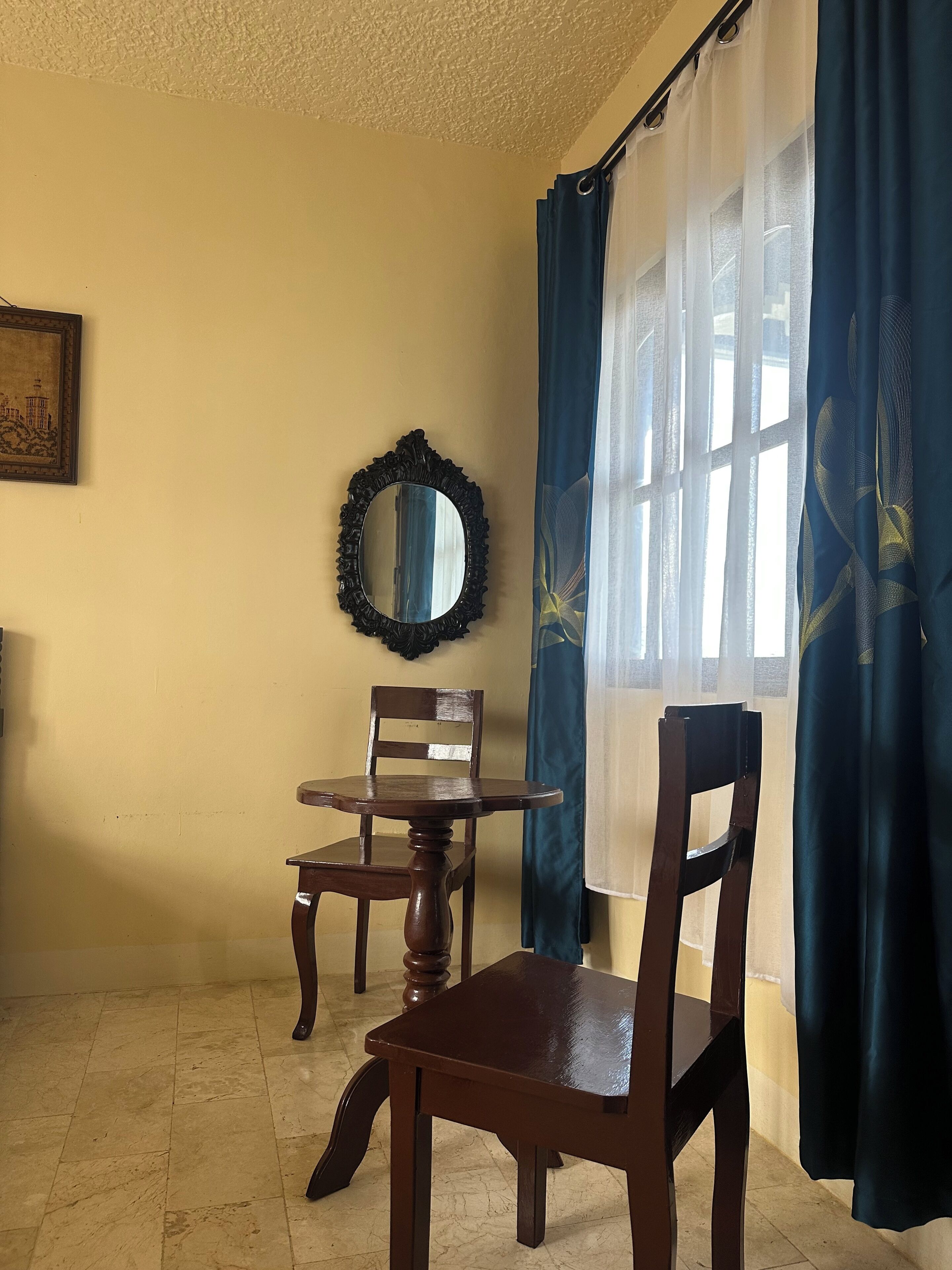 A room with a wooden chair, a small table, a mirror, and a window with curtains.