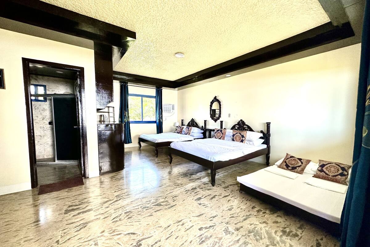 A bedroom with a large bed, a sofa, a mirror, and a window.