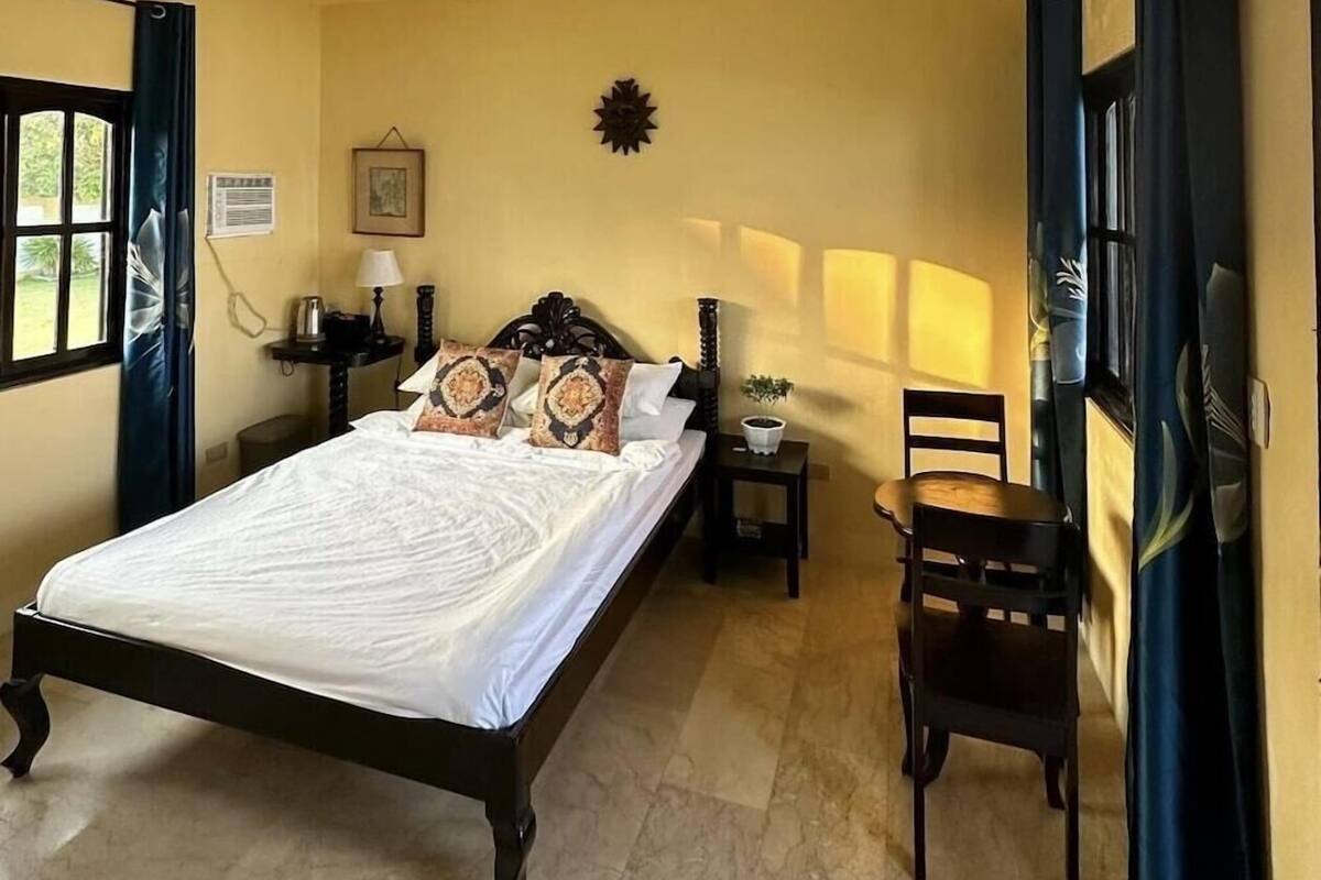 A bedroom with a bed, a chair, a nightstand, a lamp, and a wall-mounted decoration.