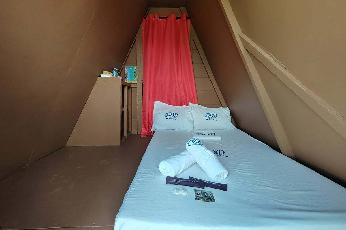 A small, triangular room with a bed, red curtains, and a small table with toiletries.