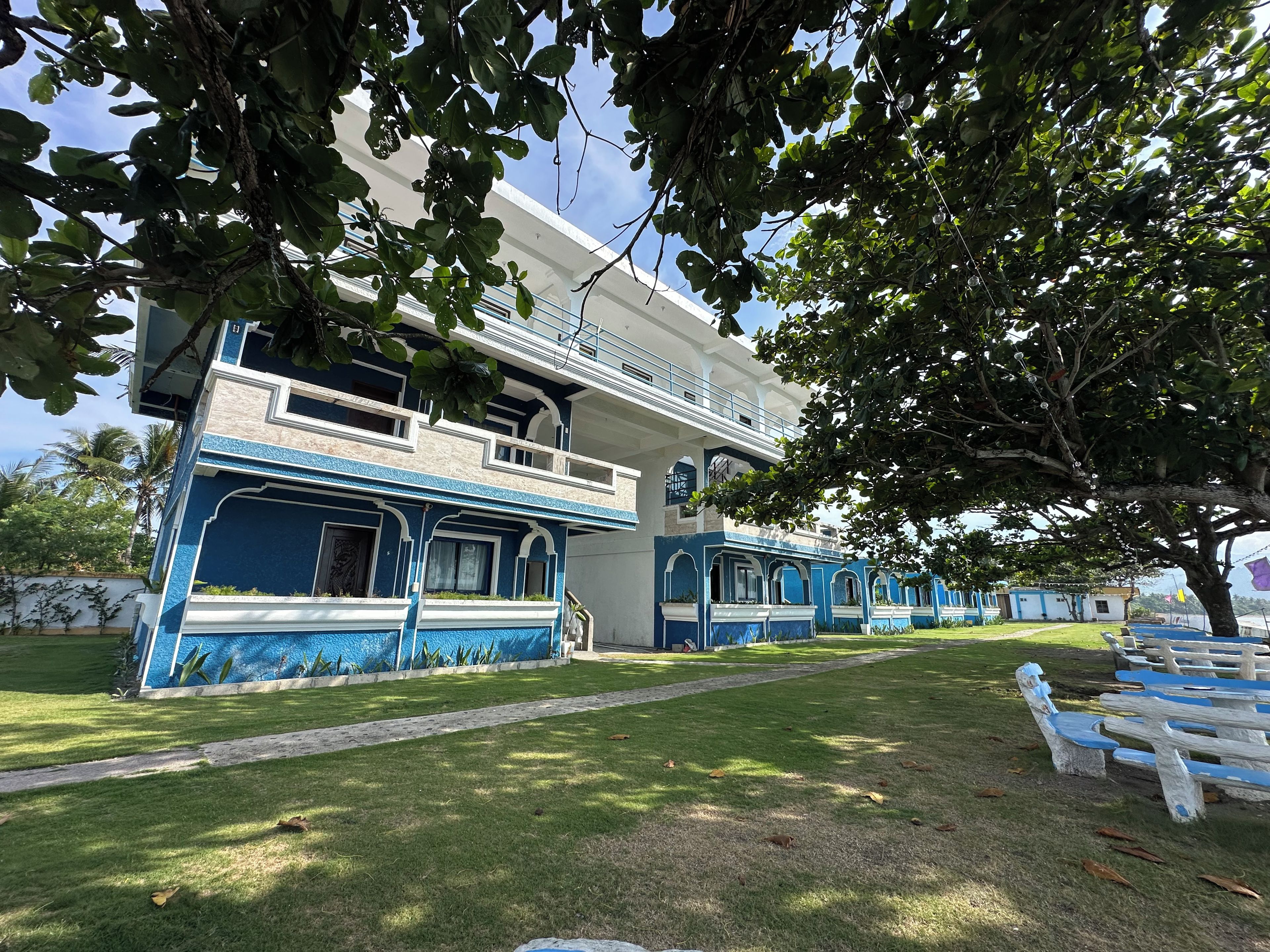 A building with a blue and white facade, a balcony, and a lawn with benches.