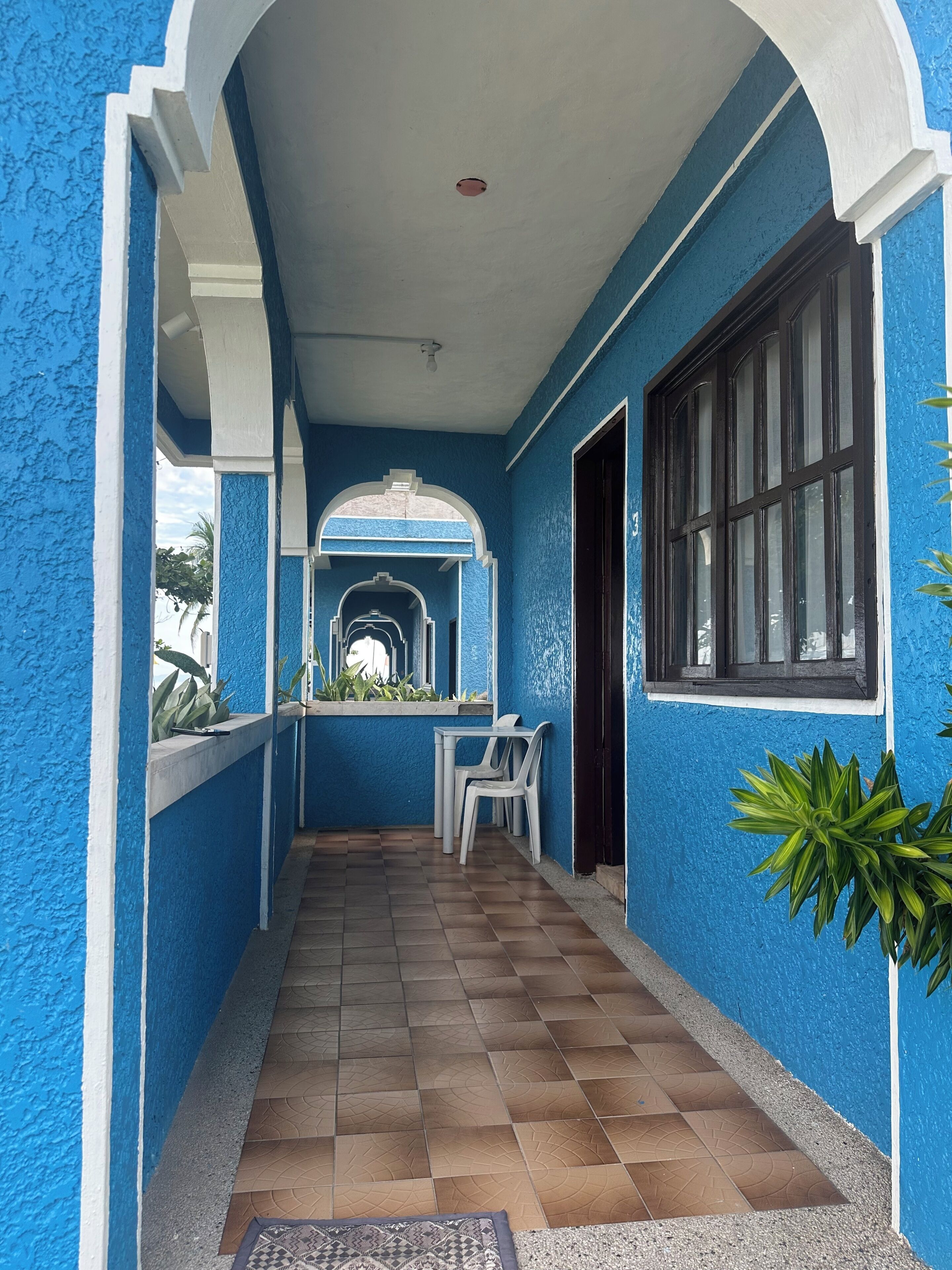 A corridor with blue walls, a tiled floor, and a window with dark frames.
