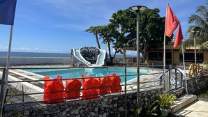 A pool area with a stone wall, a slide, and a view of the ocean. - Emmalyn's Paradise Resort (San Andres)