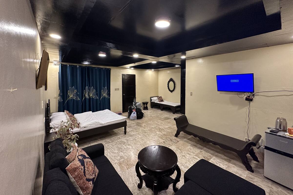 A hotel room with a bed, a sofa, a small table, a TV, and a desk with a kettle.
