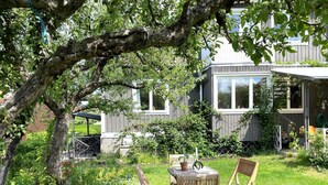 A wooden deck with a table and chairs, surrounded by lush greenery and a large tree. - 4 Person Holiday Home in Linkoping (Linkoping)