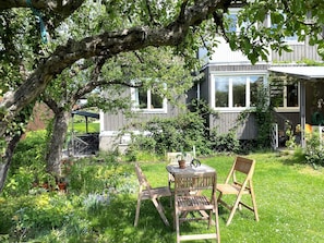 A wooden deck with a table and chairs, surrounded by lush greenery and a large tree.