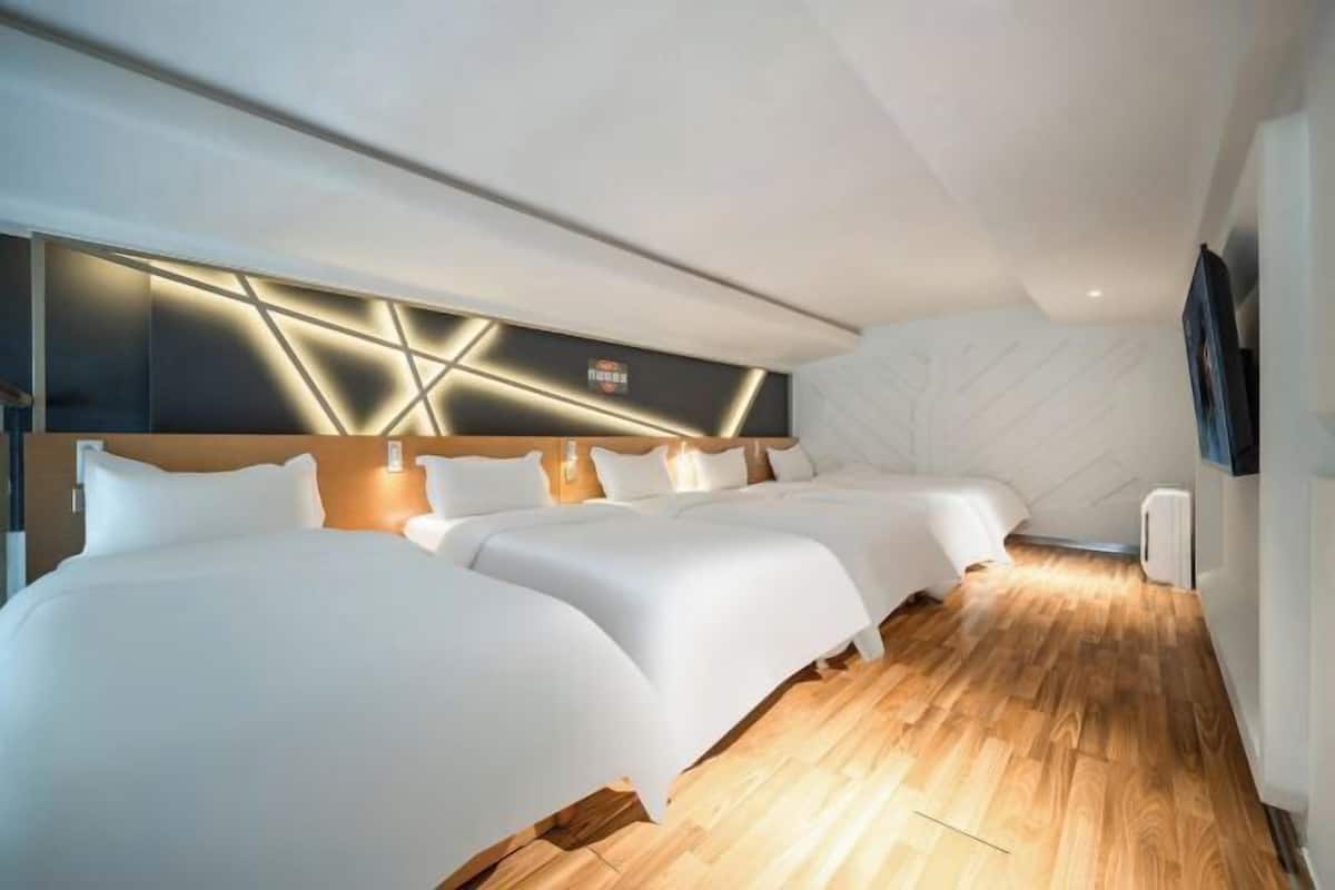 Une chambre d’hôtel avec trois lits, une tête de lit moderne et un plancher en bois.