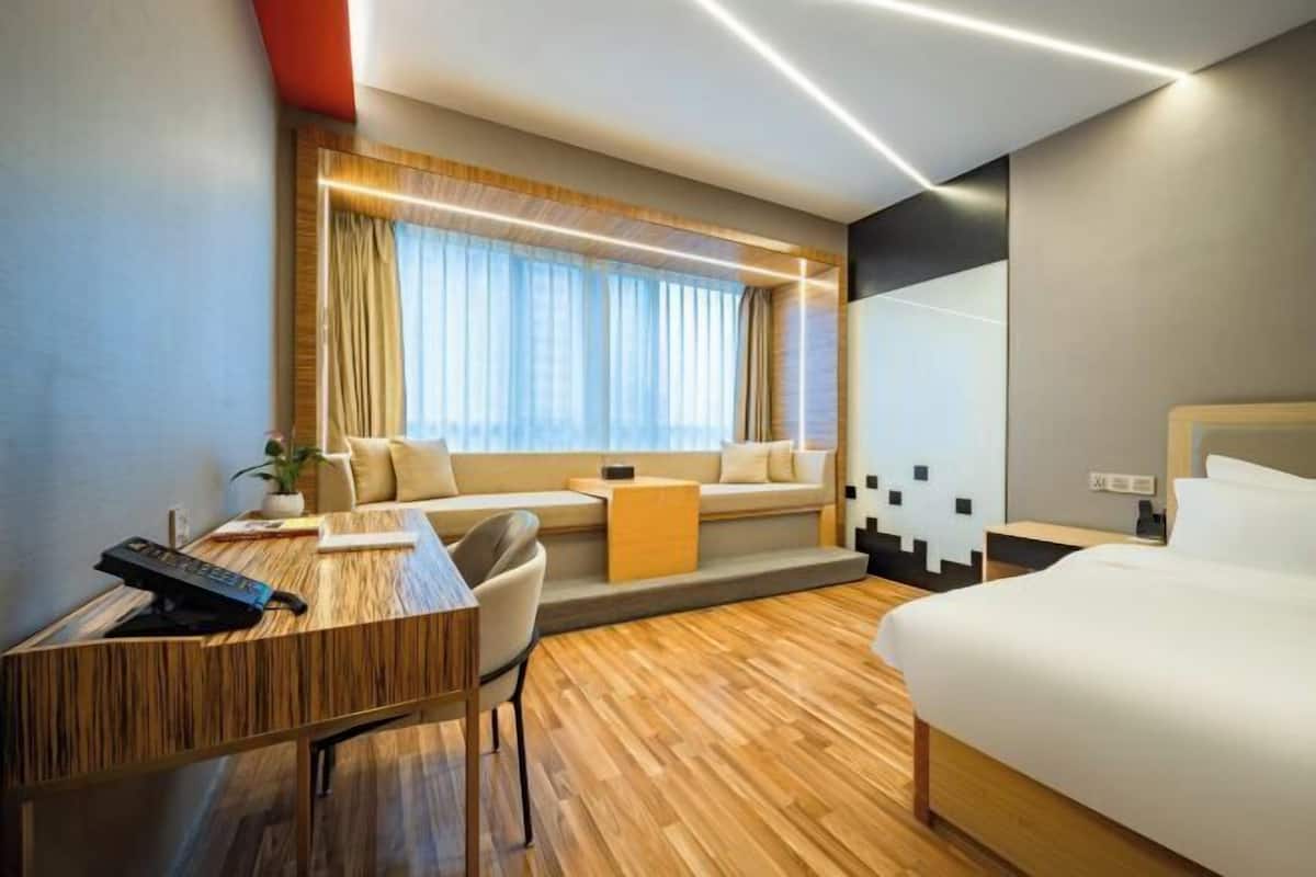 Une chambre d’hôtel moderne avec un bureau en bois, un canapé confortable, un lit et une grande fenêtre avec des rideaux.