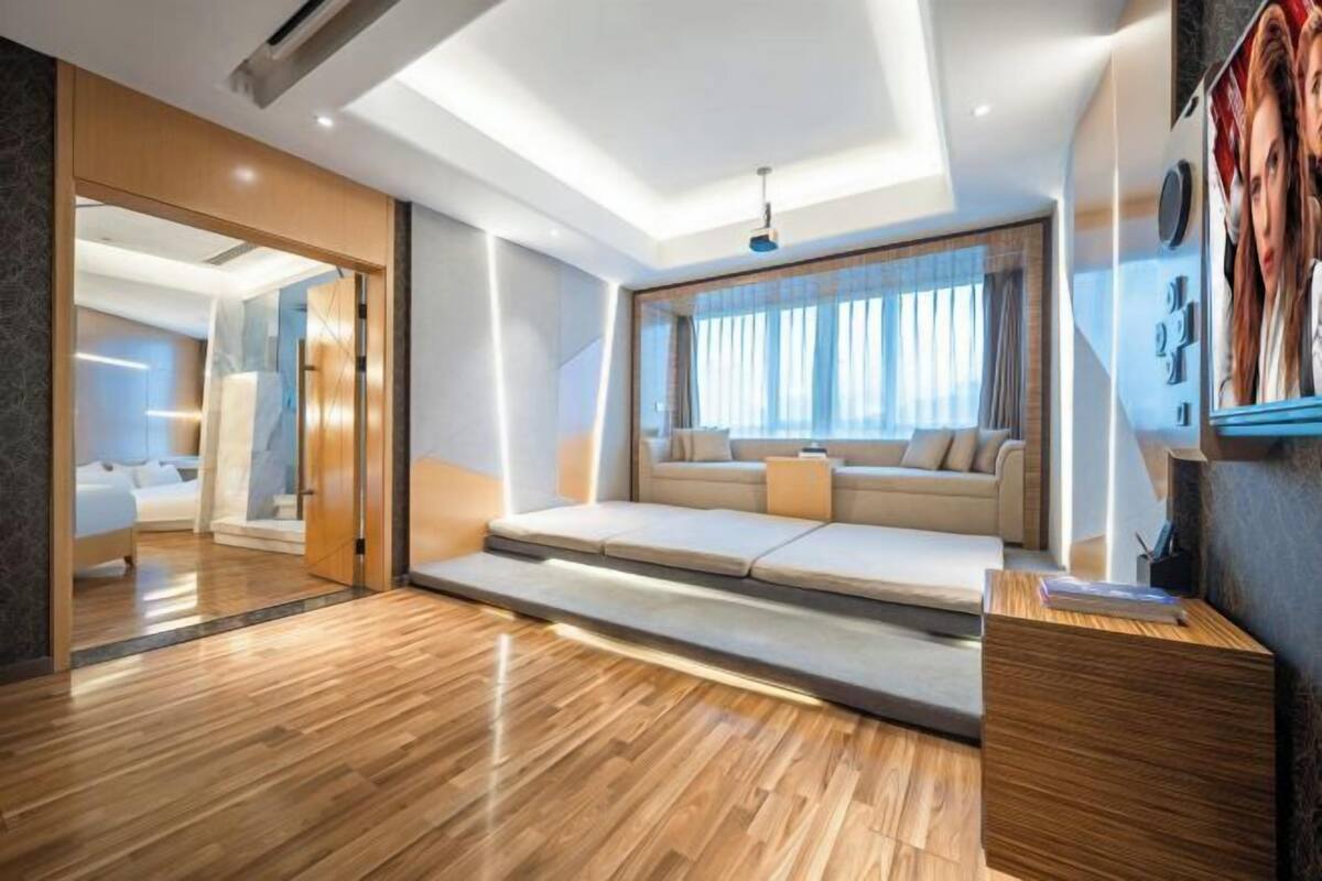 Une chambre d’hôtel moderne avec un plancher en bois, un canapé-lit, un bureau et une grande fenêtre avec des rideaux.