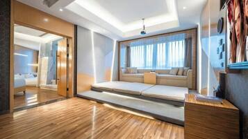 A modern hotel room with a wooden floor, a sofa bed, a desk, and a large window with curtains.