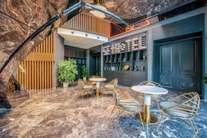 Un interior moderno con piso de mármol, una zona de estar con mesas y sillas redondas, y una estantería con objetos decorativos.