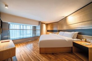 Une chambre d’hôtel moderne avec un grand lit, un plancher en bois, une table de chevet, une lampe de chevet et une grande fenêtre avec des rideaux.