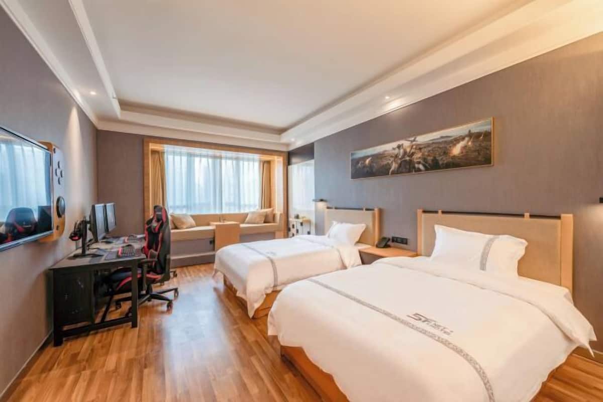 Une chambre d’hôtel avec deux lits, un bureau avec un ordinateur, une télévision et une fenêtre avec des rideaux.