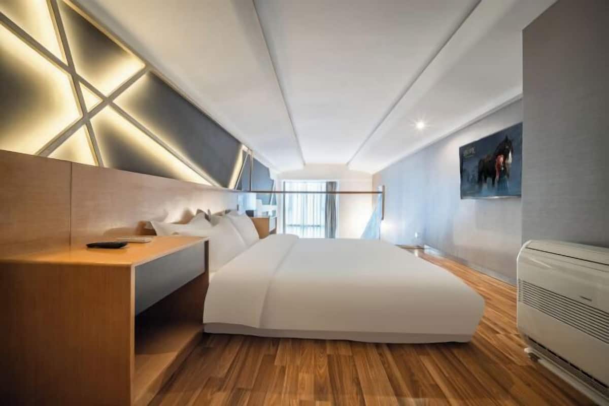 Une chambre d’hôtel moderne avec un grand lit, un bureau en bois et un climatiseur fixé au mur.