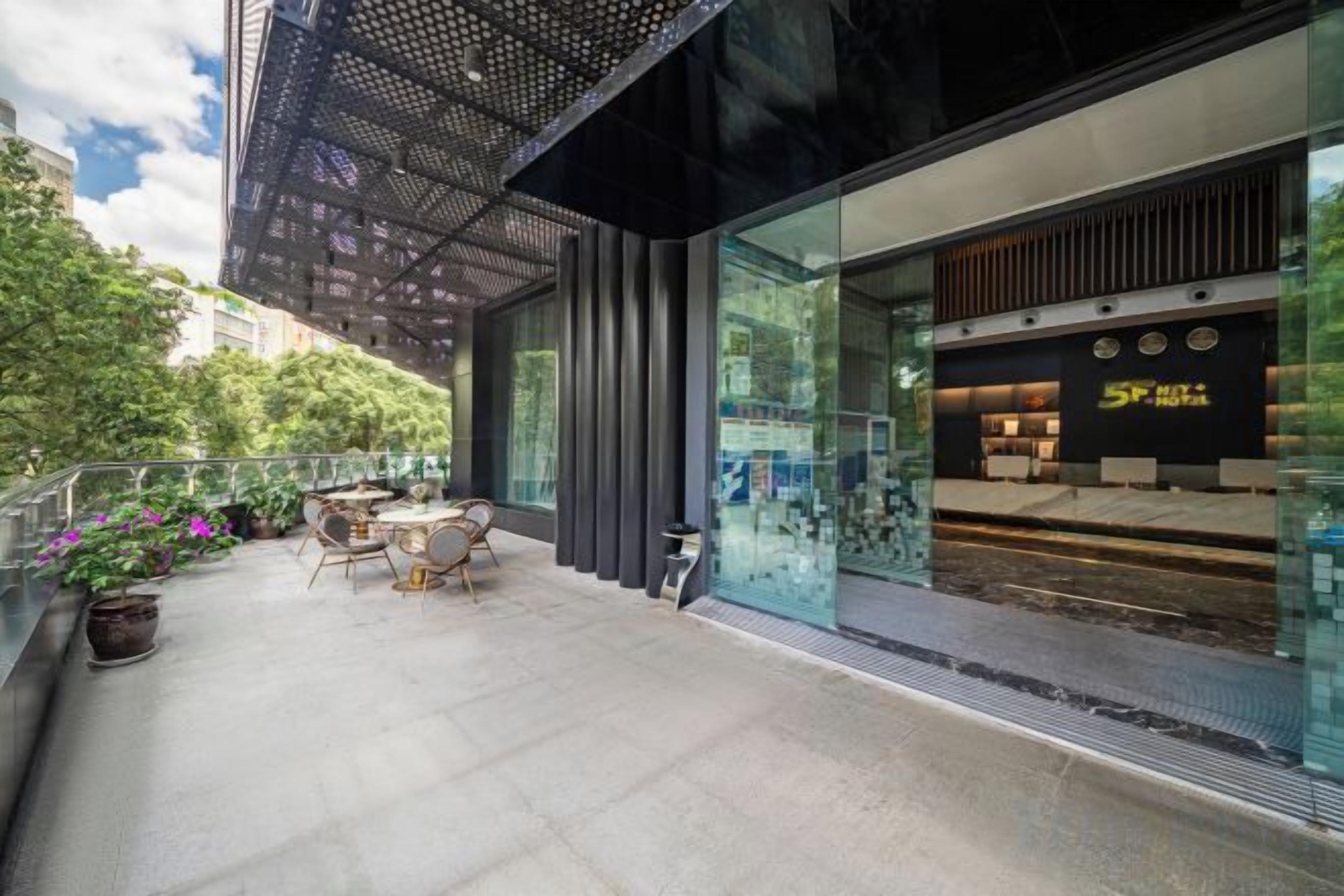 An outdoor seating area with tables and chairs, a glass storefront, and a modern building facade.