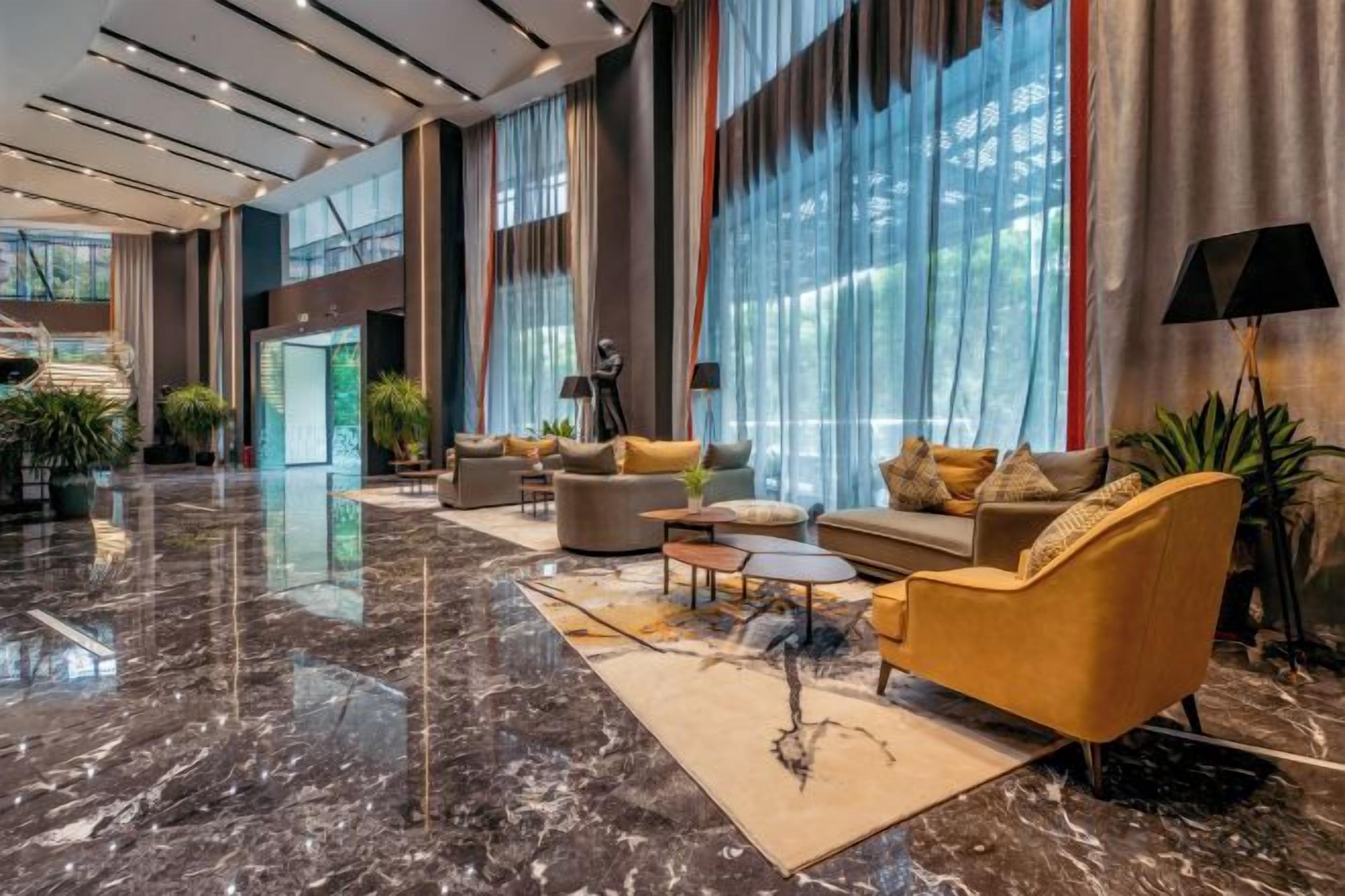 A spacious lobby with a marble floor, comfortable seating, large windows, and indoor plants.