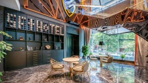 A modern interior with a marble floor, a round table with chairs, a bookshelf with various items, and a large window with a view of greenery. - Guiyang Wufang Zhixuan Hotel (Guiyang)
