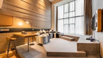 A modern living room with a sofa set, a coffee table, a bar area, and a large window providing natural light.