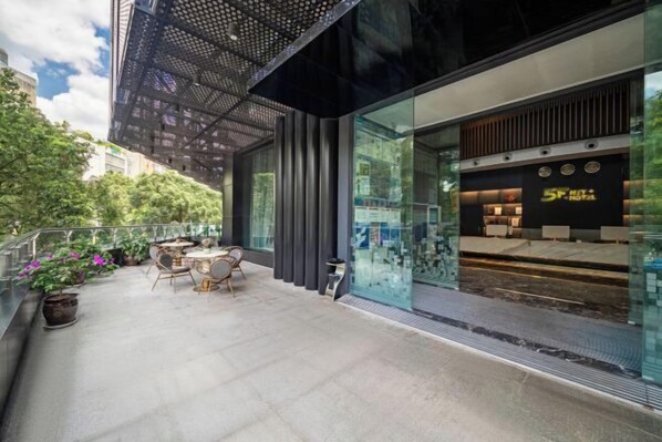 Un hôtel moderne doté d’une façade en verre, d’un espace extérieur aménagé et offrant une vue sur le paysage urbain environnant.