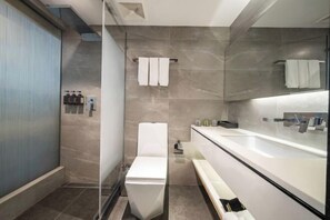 Een moderne badkamer met een douchecabine van glas, een wit toilet, een grote spiegel en een wastafelmeubel met een wastafel.