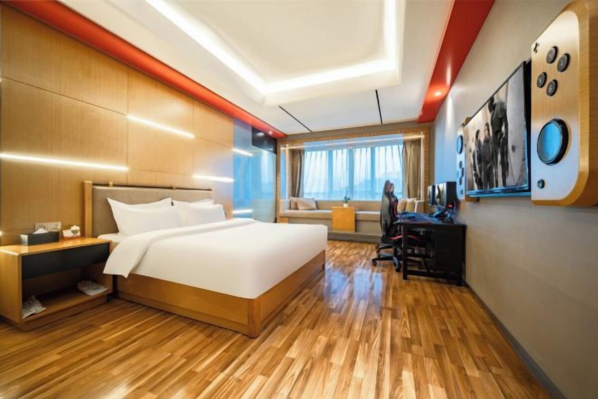 Habitación de hotel moderna con piso de madera, una cama grande, un escritorio y una ventana con cortinas.