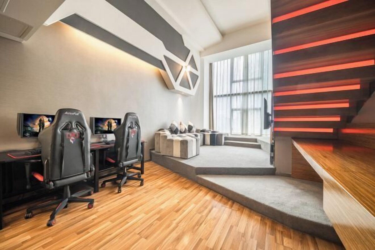 Een moderne gamekamer met twee gaming stoelen, een groot scherm en een gezellige zithoek met een trap naar een balkon.