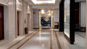 A modern hotel lobby with a marble floor, a central art piece, and a glass elevator. - Vienna International Hotel (Wenzhou Avenue Railway Store) (Wenzhou)