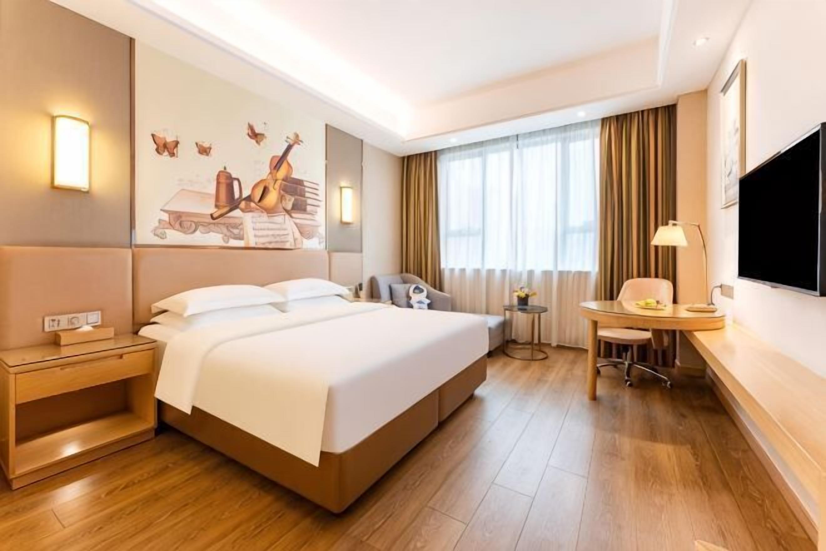 A hotel room with a large bed, a desk with a chair, a television, and a window with curtains.