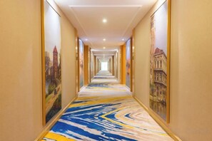 A hotel corridor with a patterned carpet, framed artwork on the walls, and a long, straight path leading to the end. - Vienna International Hotel (Wenzhou Avenue Railway Store) (Wenzhou)