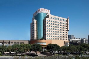 A multi-story hotel with a prominent curved glass facade, a flat roof, and a parking lot in the foreground. - Vienna International Hotel (Wenzhou Avenue Railway Store) (Wenzhou)