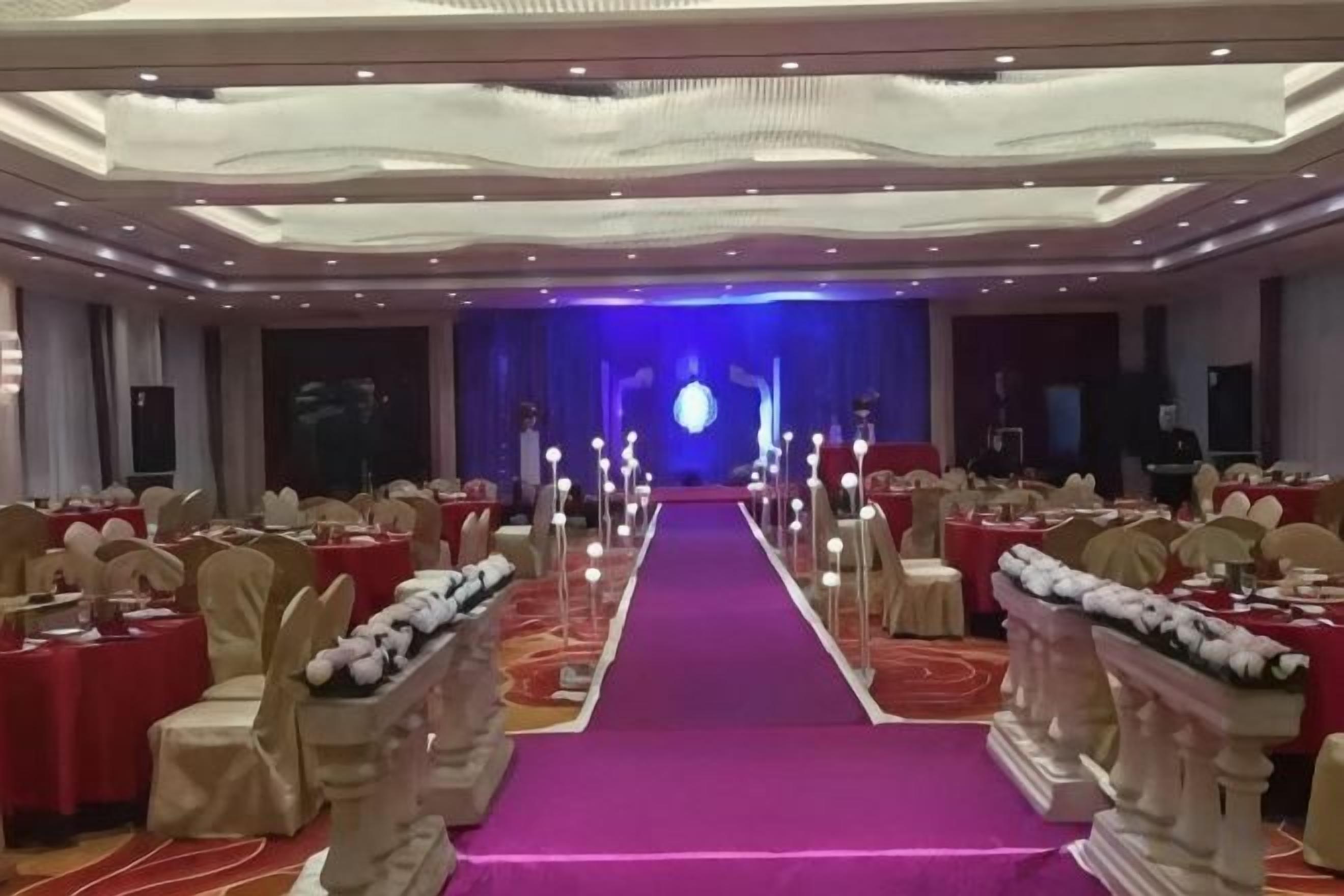 A banquet hall with a central aisle, rows of tables, and chairs.