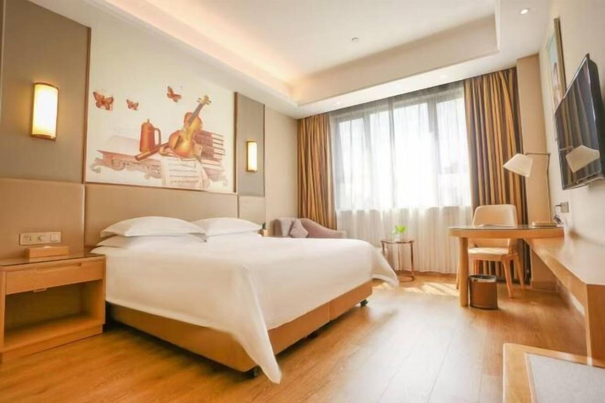 Habitación de hotel con cama, mesita de noche, escritorio, silla y un amplio ventanal con cortinas.