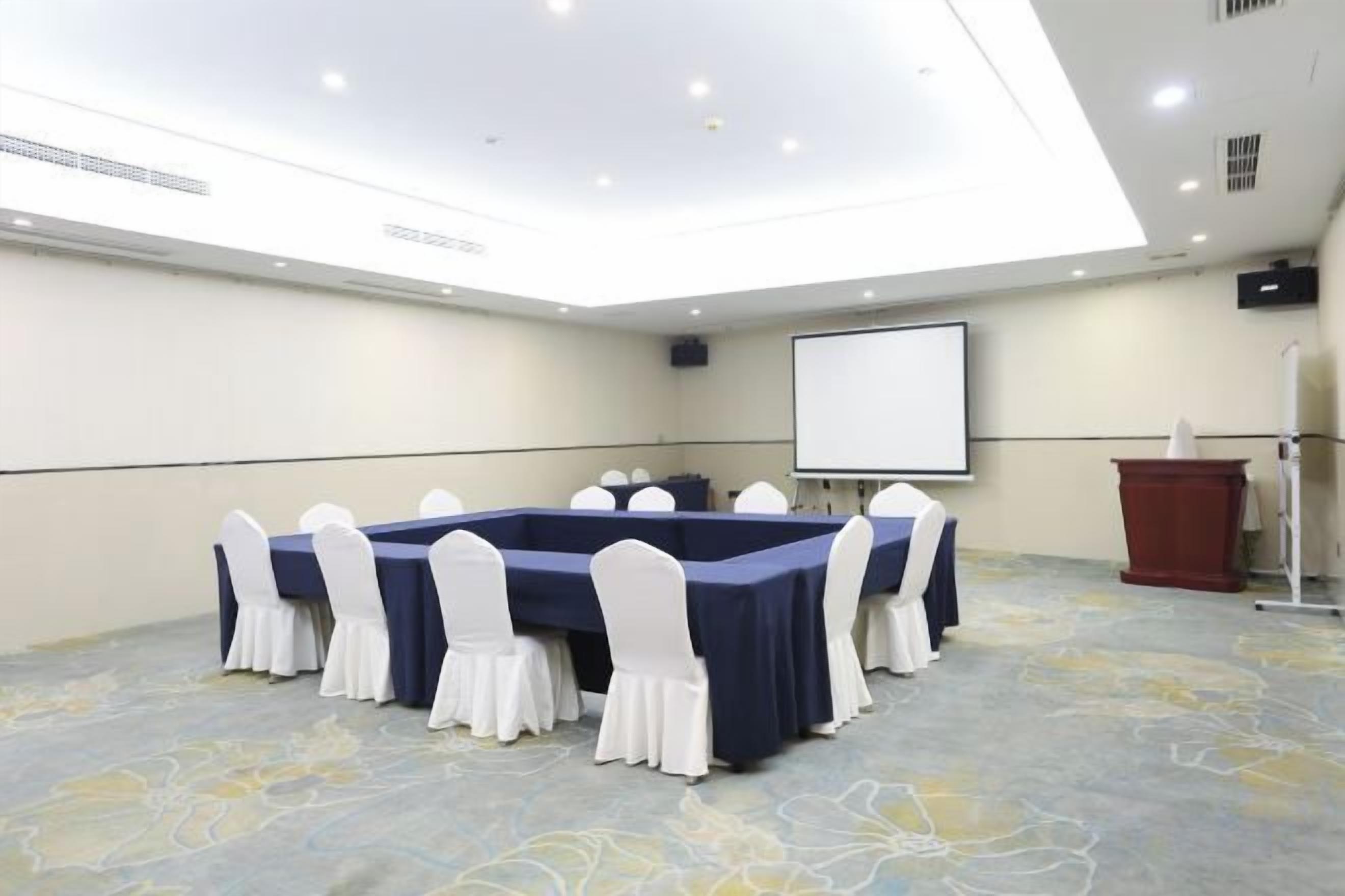 A conference room with a long table, white chairs, a projector screen, and a podium.