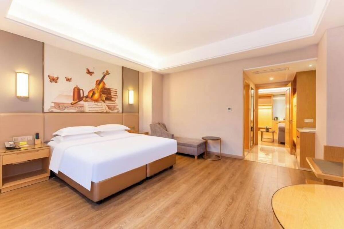 Una habitación de hotel con una cama grande, mesitas de noche, un pequeño sofá, una mesa redonda y un cuadro en la pared.