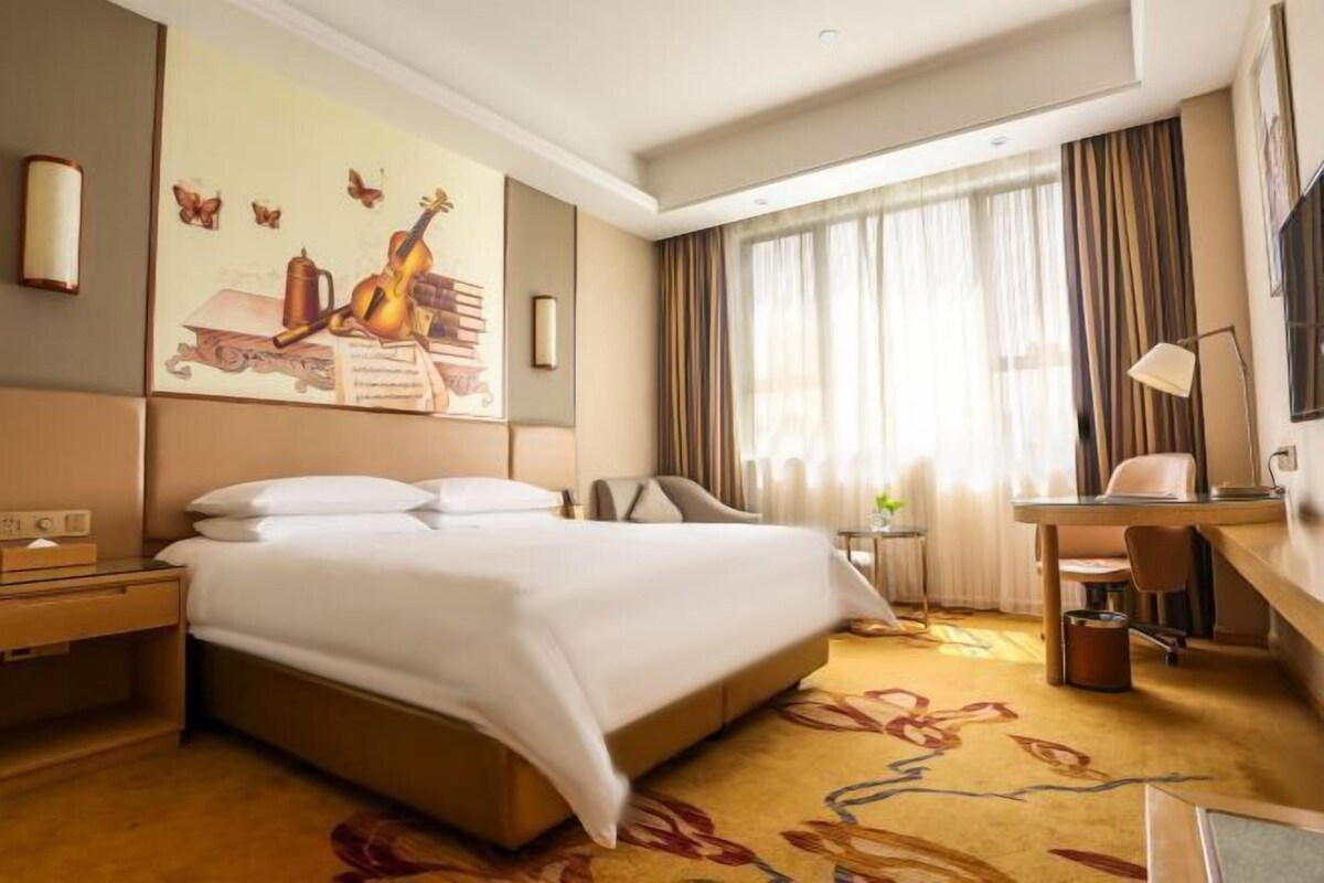 Ein Hotelzimmer mit einem großen Bett, einem Schreibtisch, einem Stuhl, einer Lampe und einem Bild an der Wand.