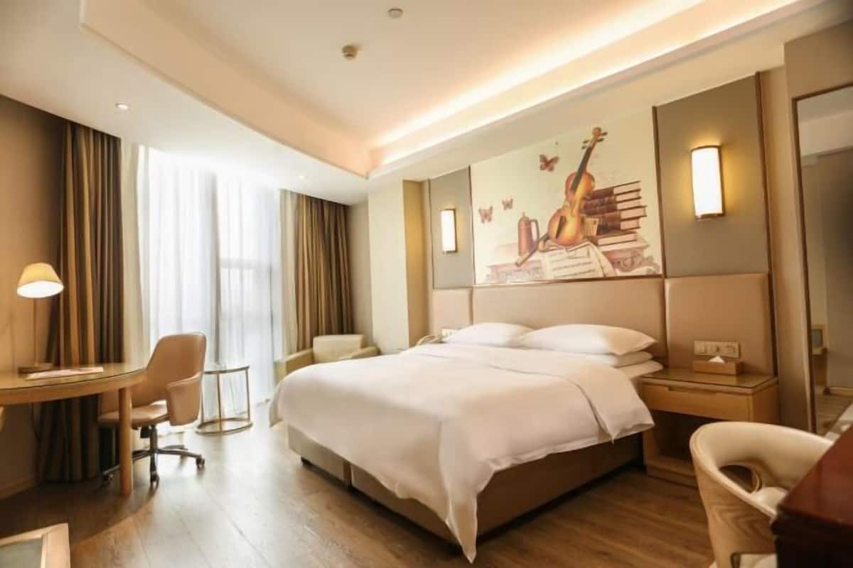 Una habitación de hotel con cama, escritorio, silla y un cuadro en la pared.
